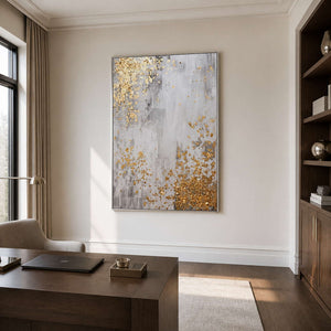 Silver framed gray and gold abstract artwork above a desk beside dark bookshelves.