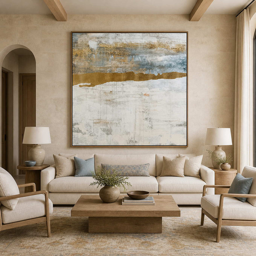 Wood framed pale abstract horizon above a cream sofa with muted blue cushions.