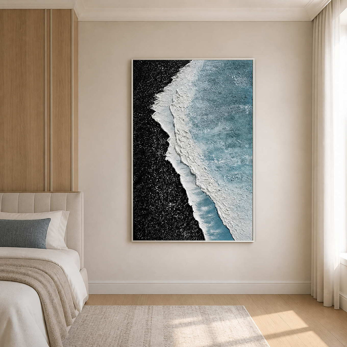 White framed shoreline abstract beside a cream bed with a blue cushion.