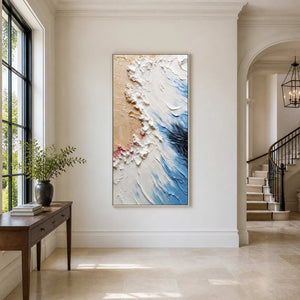 Silver-framed blue and beige textured artwork beside a bright entryway staircase and wooden console.
