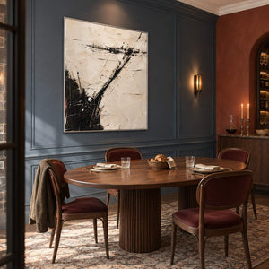 Ivory abstract painting with sweeping black marks and fine crossing lines in a silver frame in a dining room.