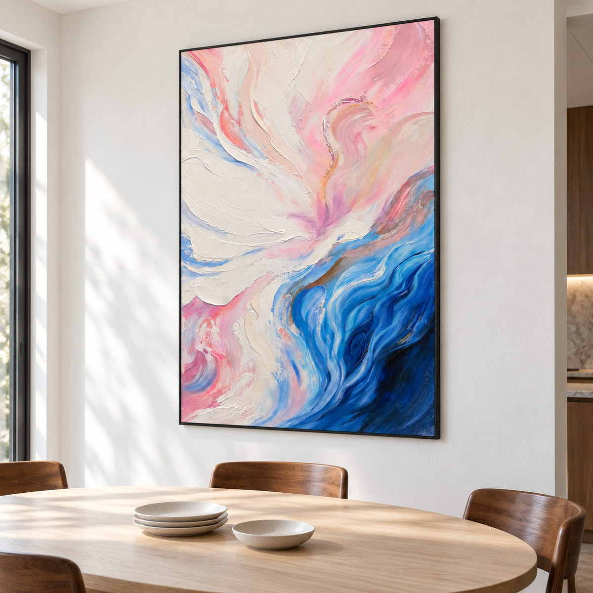 In a dining area beside the table, an artwork with a black frame shows cream and pink folds flowing into deep blue curves at the lower right.