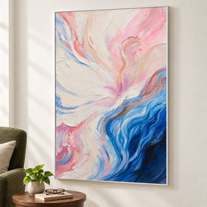 Cream and pink folds flowing into deep blue curves at the lower right in an artwork with a white frame, displayed beside a reading chair.
