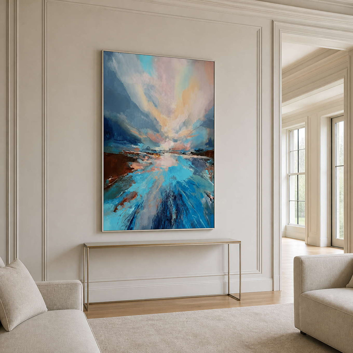 Silver framed blue landscape above a slim console between cream living room chairs.