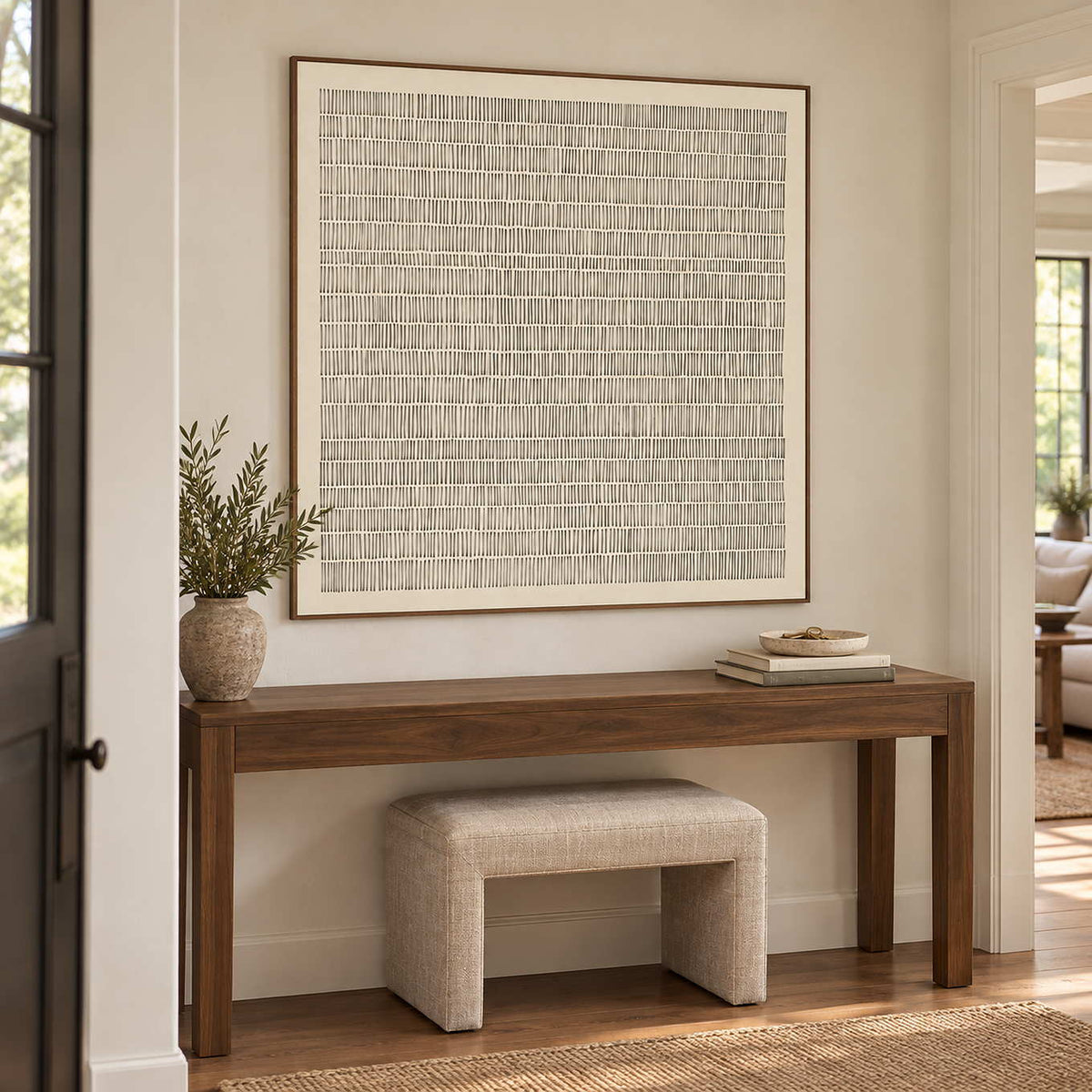 Slow and Lasting in a wood frame above a dark hallway console with a leafy vase and a cream stool below.