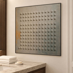 A regular grid of raised round forms on a gray earth-toned ground in a black frame, displayed in a bathroom dry area.