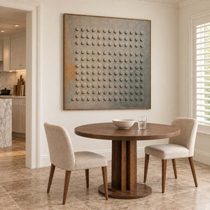 A regular grid of raised round forms on a gray earth-toned ground in a brown wood frame, displayed above a dining table.