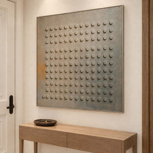 A regular grid of raised round forms on a gray earth-toned ground in a silver frame, displayed above an entryway console.