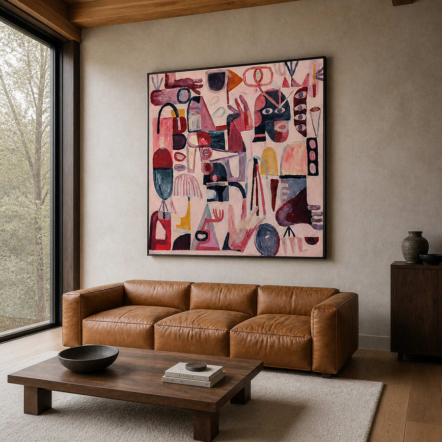 Black framed pink abstract symbol painting above a leather sofa in a bright living room.