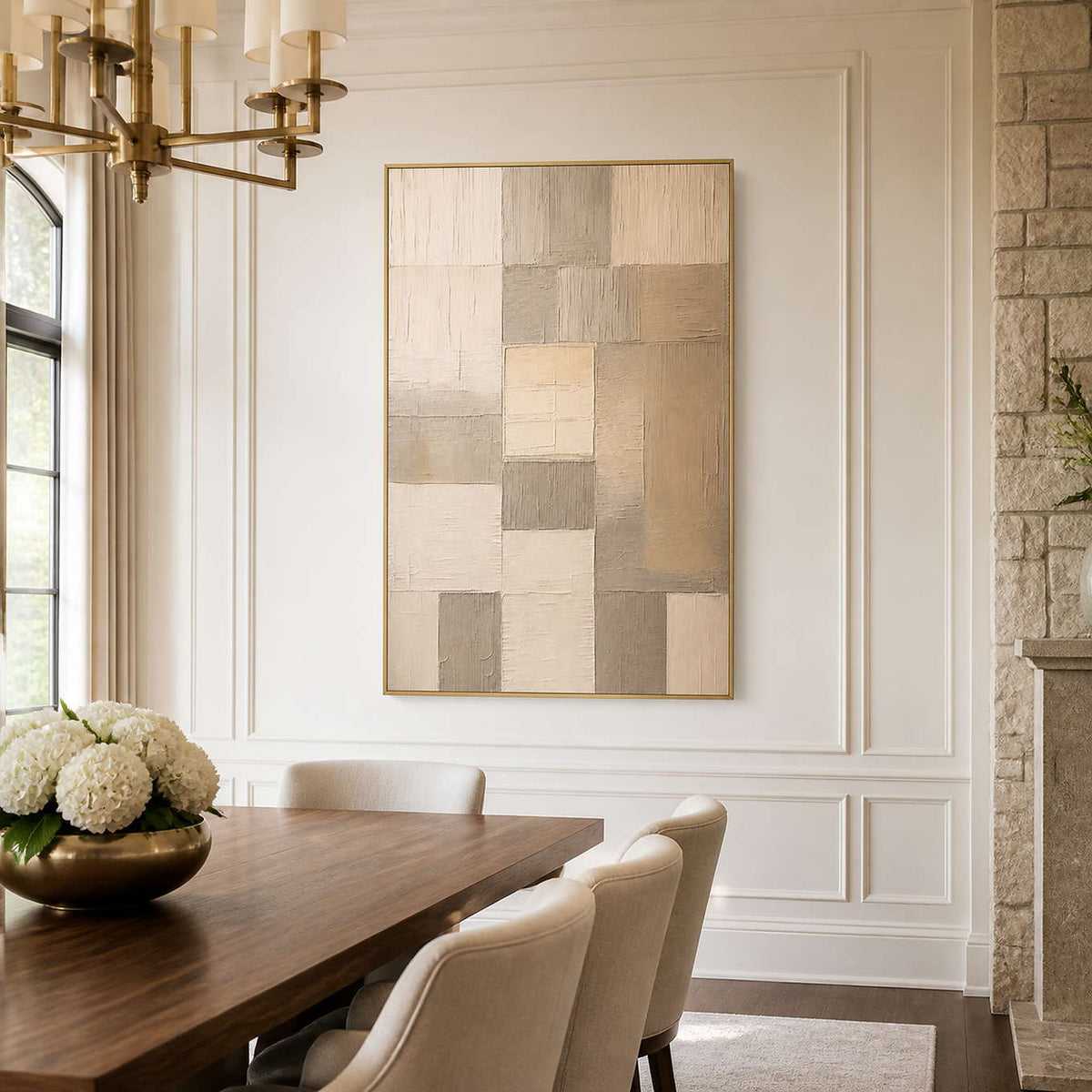 Gold framed neutral geometric artwork beside a dining table and cream chairs.