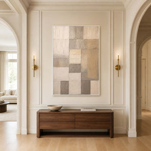 White framed neutral patchwork artwork above a walnut console between brass sconces.