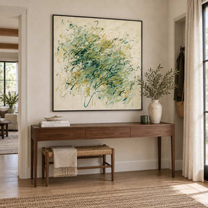 Spring Comes Calling in a black frame above a wood console and woven-seat bench in an entryway.