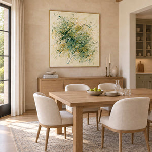 Spring Comes Calling in a gold frame above a light wood sideboard behind a dining table with cream chairs.