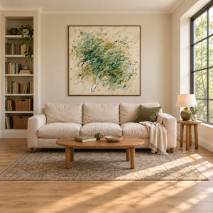Spring Comes Calling in a wood frame above a cream sofa beside bookshelves and a tall sunlit window.