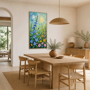 Gold-framed floral painting beside a wooden dining table beneath a woven pendant light.