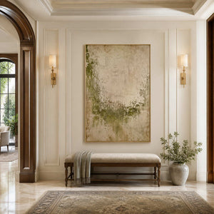 Gold framed pale green abstract painting above an upholstered bench in a bright hallway.