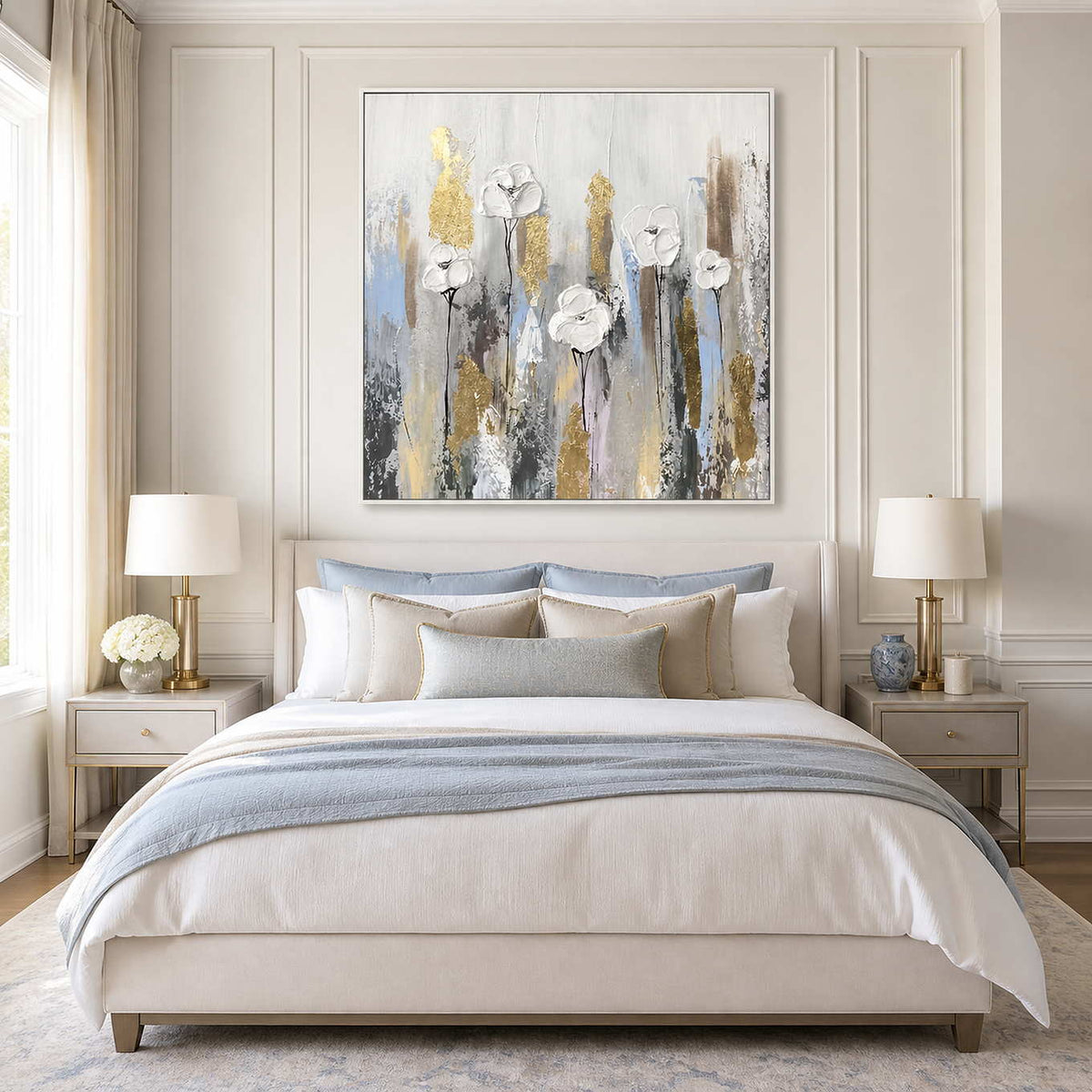 White framed floral painting above a cream bed with pale blue pillows and brass lamps.