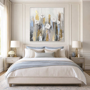 White framed floral painting above a cream bed with pale blue pillows and brass lamps.