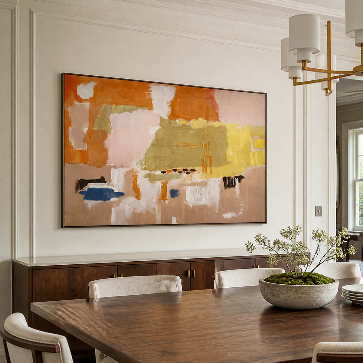 Black framed warm abstract artwork above a sideboard beside a wooden dining table.