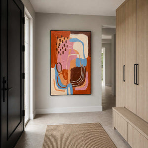 Black framed abstract painting beside an entry door and pale wooden cabinets.