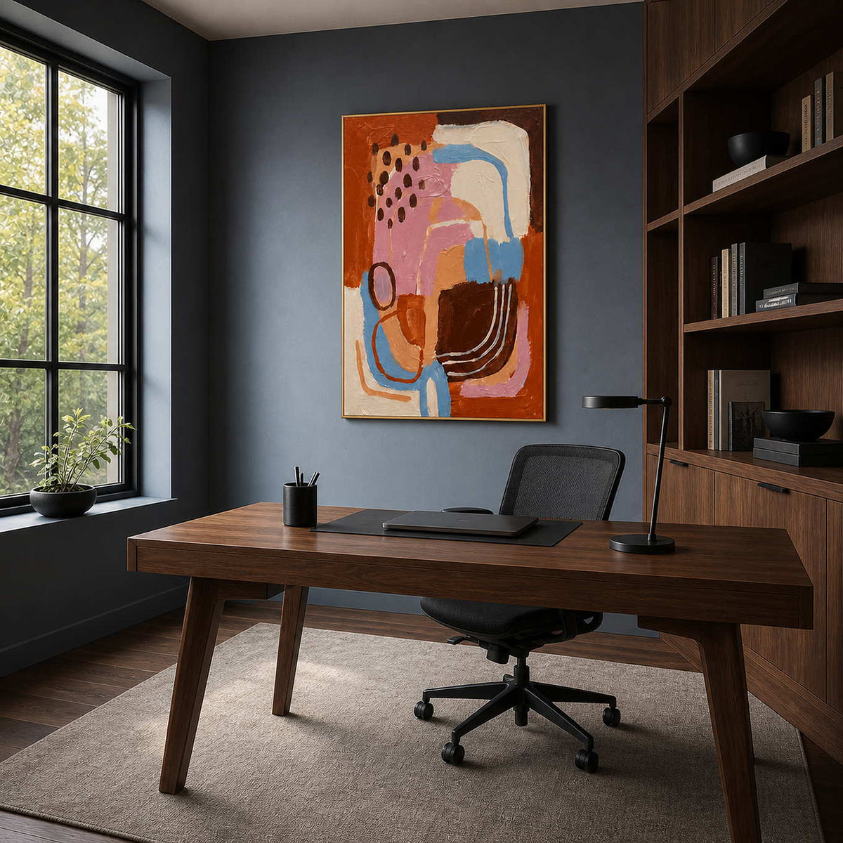 Gold framed colorful artwork above a walnut desk against a dark office wall.