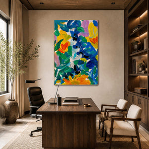 Silver framed bright floral artwork behind a wooden office desk beside dark built-in shelving.