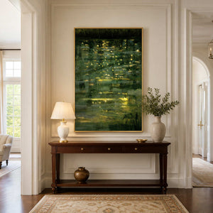 Gold framed green reflection painting above a hallway console with a lamp and vase.