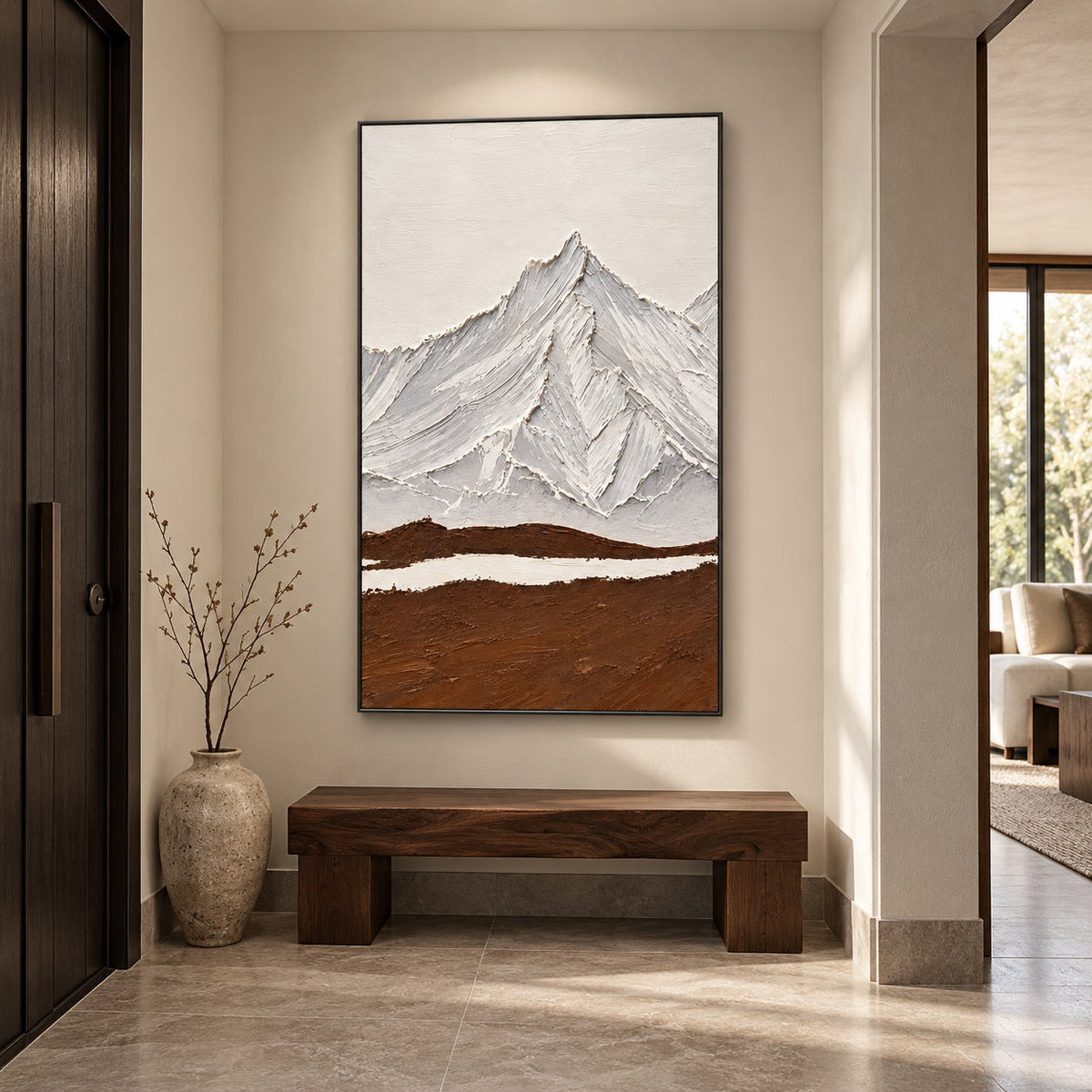White and gray ridged mountains above a broad brown foreground and a narrow white band in an artwork with a black frame, displayed in an entryway above a console or bench.