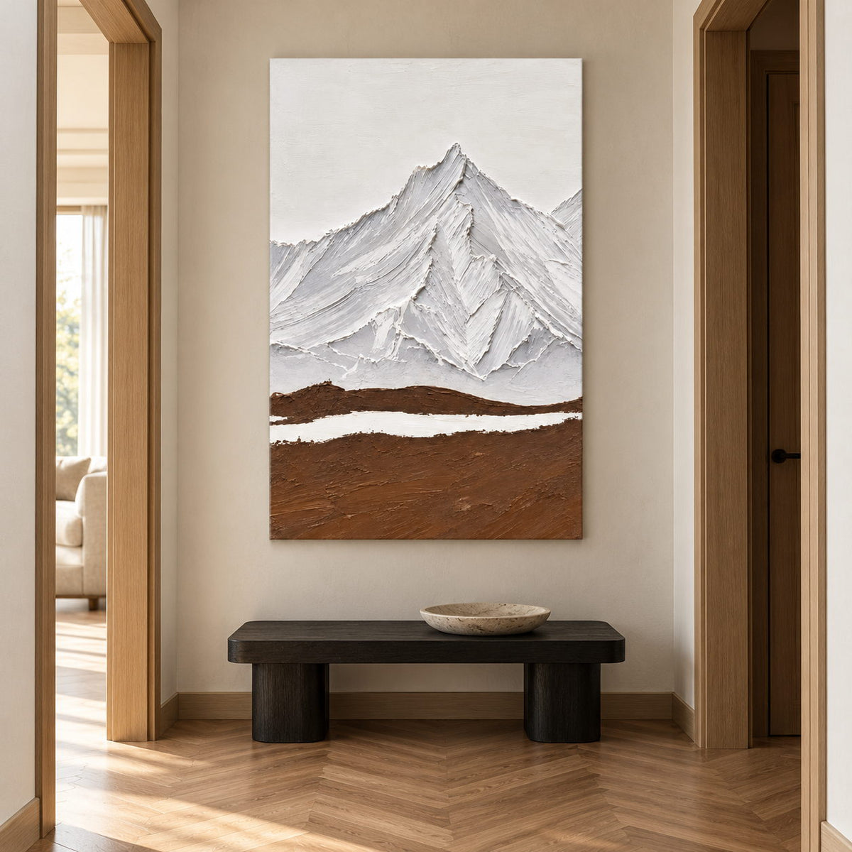 In a hallway above a bench, an artwork with no outer frame shows white and gray ridged mountains above a broad brown foreground and a narrow white band.