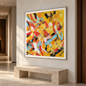 Artwork showing interlocking yellow, orange, light blue, white and black abstract strokes in a hallway above a bench, with a silver-colored frame.