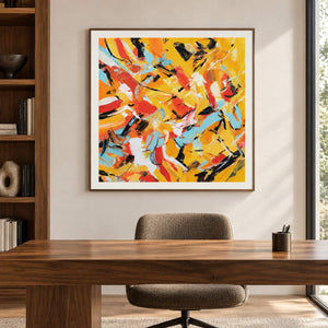 In a study with a desk, an artwork with a brown wood-look frame shows interlocking yellow, orange, light blue, white and black abstract strokes.