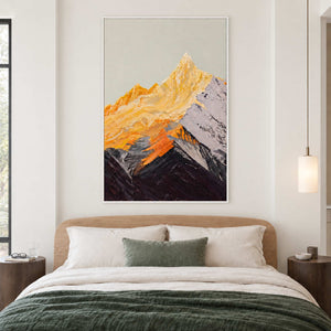 White-framed golden mountain artwork above a wooden bed with white pillows and a dark green cover.