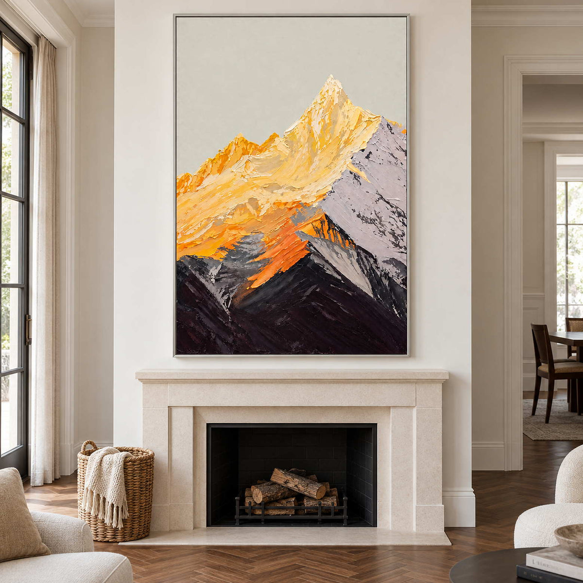 Silver-colored framed mountain artwork above a pale fireplace, its golden upper slopes contrasting with dark foreground ridges.