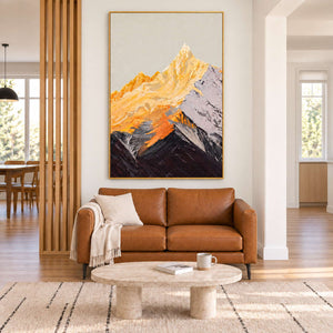 Golden mountain artwork in a gold-colored frame above a tan sofa, with a wood-slat divider and light oval coffee table in the living room.