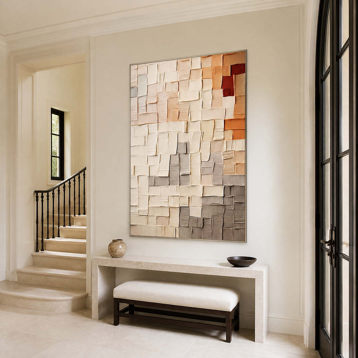 Silver-framed cream and peach grid artwork above a stone console near an entryway staircase.