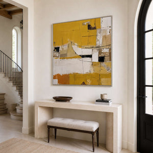 Silver-framed yellow and cream artwork above a stone console beside an entryway staircase.