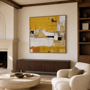 Wood-framed yellow and cream artwork above a cabinet beside a library lounge reading chair.