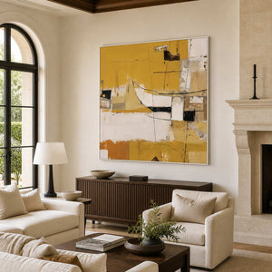 White-framed yellow abstract wall art above a wooden cabinet beside cream living room seating.