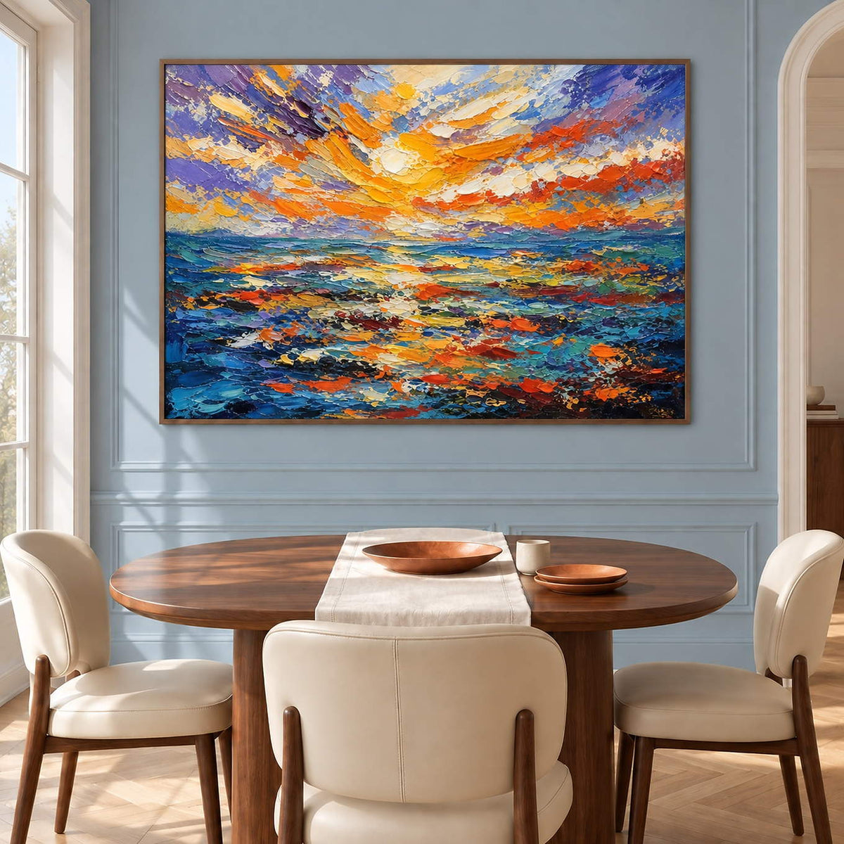 Textured seascape painting with a gold and orange sunset over blue water in a brown wood frame in a dining room.