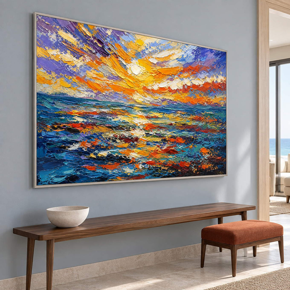Textured seascape painting with a gold and orange sunset over blue water in a silver frame in an entrance hall.