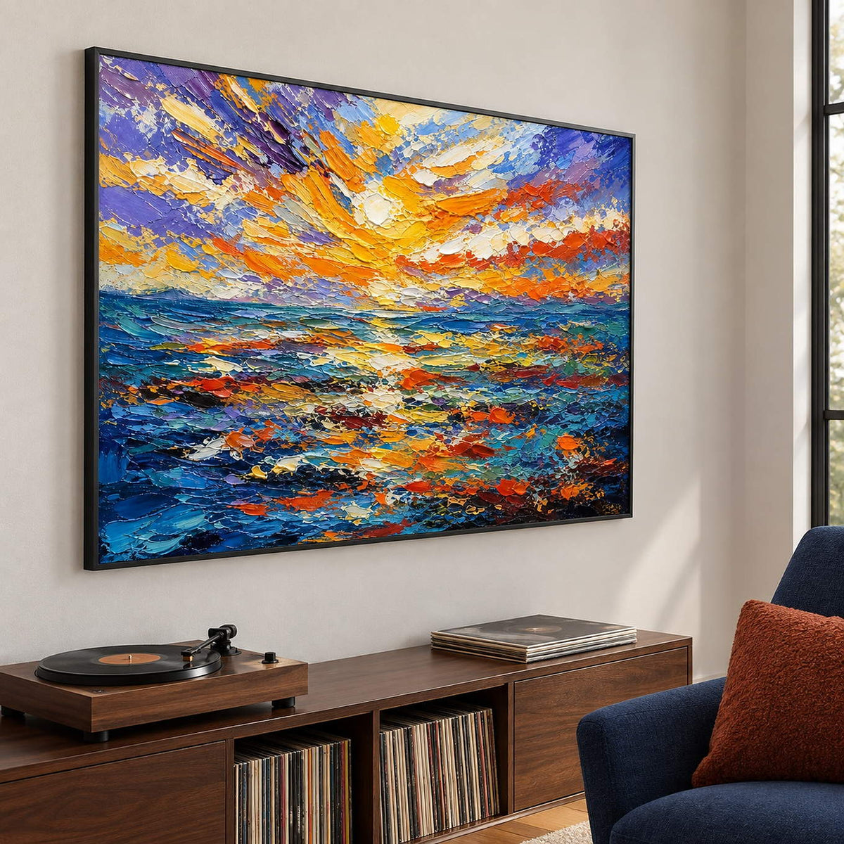 Textured seascape painting with a gold and orange sunset over blue water in a black frame in a lounge.
