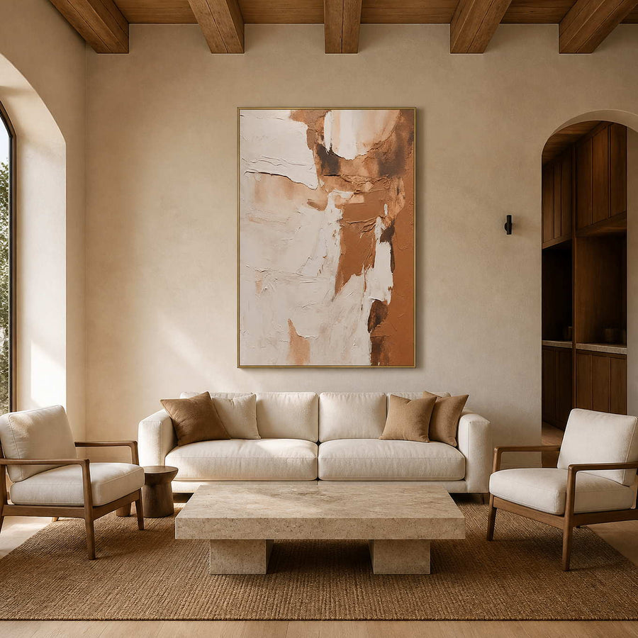 Gold framed cream and caramel abstract artwork above a sofa beneath wooden beams.