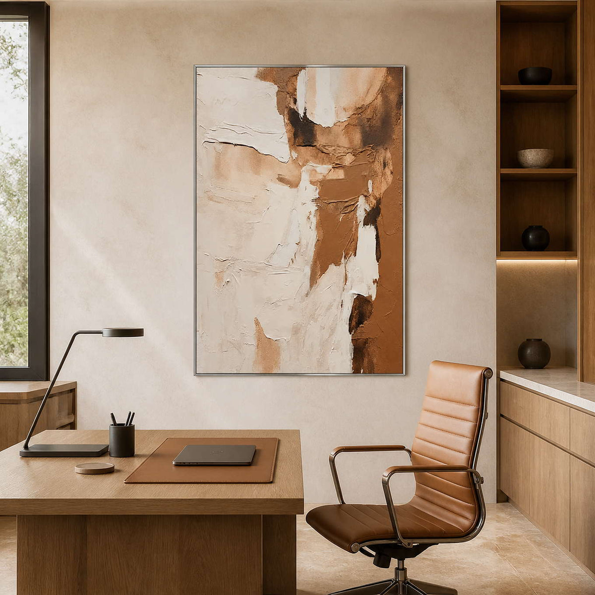 Silver framed cream and caramel artwork beside a wooden desk and leather chair.