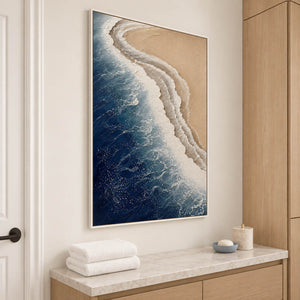 White surf curling along a sandy shore beside dark blue water in a white frame, displayed in a bathroom dry area.