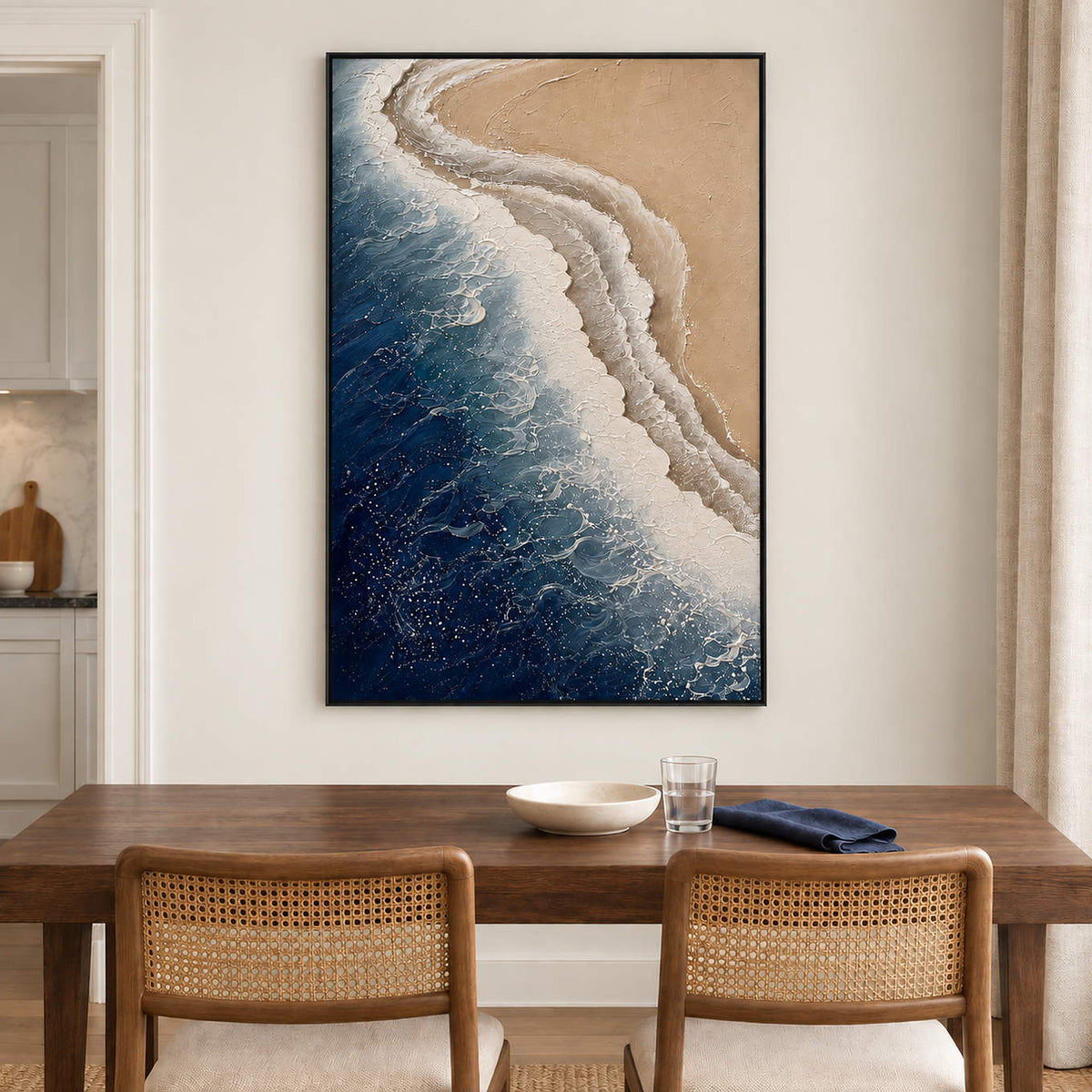 White surf curling along a sandy shore beside dark blue water in a black frame, displayed above a dining table.