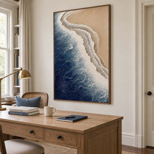 White surf curling along a sandy shore beside dark blue water in a brown wood frame, displayed in a home office.