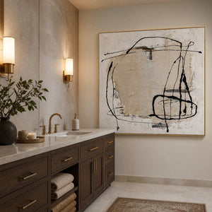 Gold-framed abstract wall art beside a stone vanity in a warm neutral bathroom.