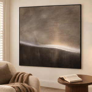 A thin glowing horizon between smoky gray and dark brown fields in a black frame, displayed beside seating in a lounge.