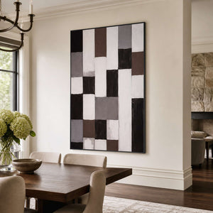 Black framed geometric abstract artwork above a wooden dining table with pale chairs and flowers.