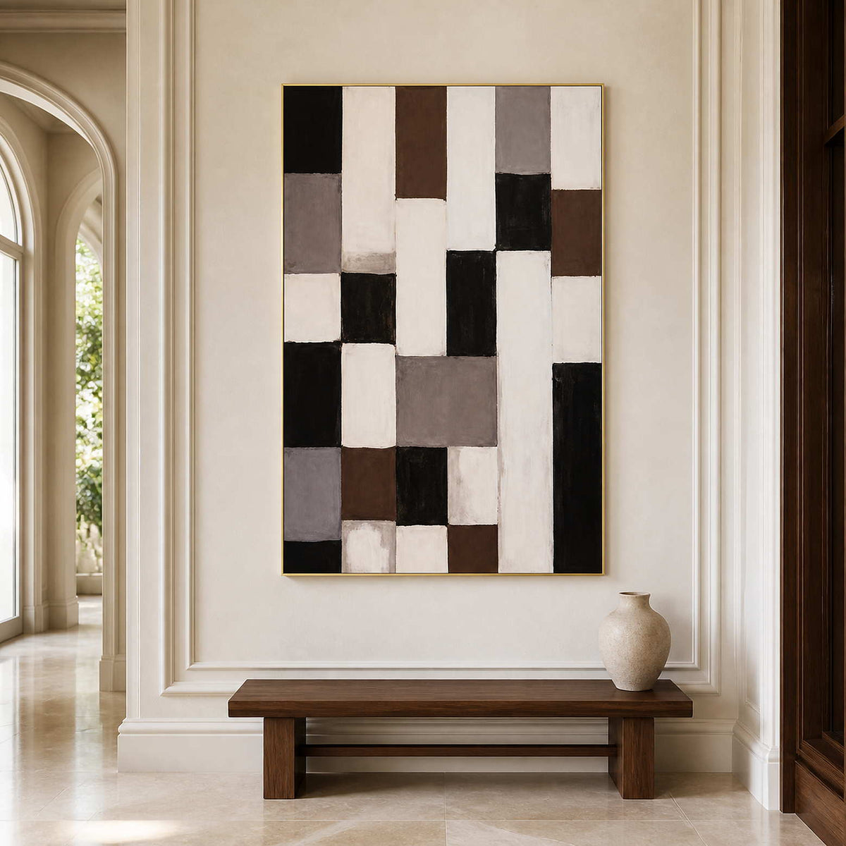 Gold framed neutral geometric artwork above a wooden bench beside an arched hallway opening.